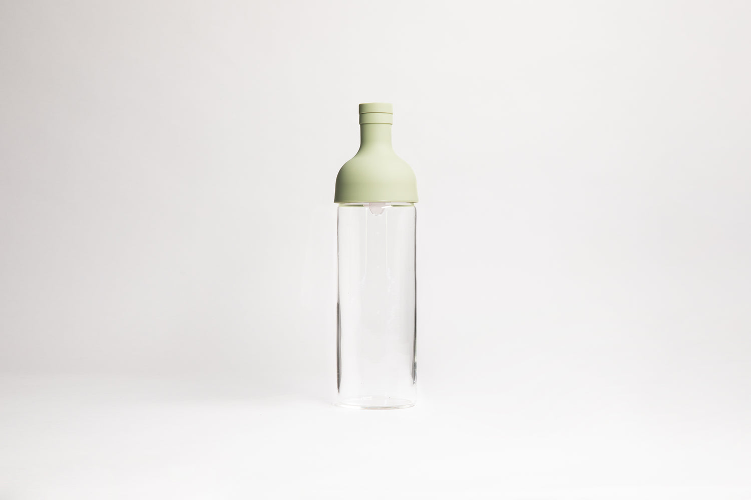 Tall glass container with light green rubber wine bottle shaped top on an white backdrop.