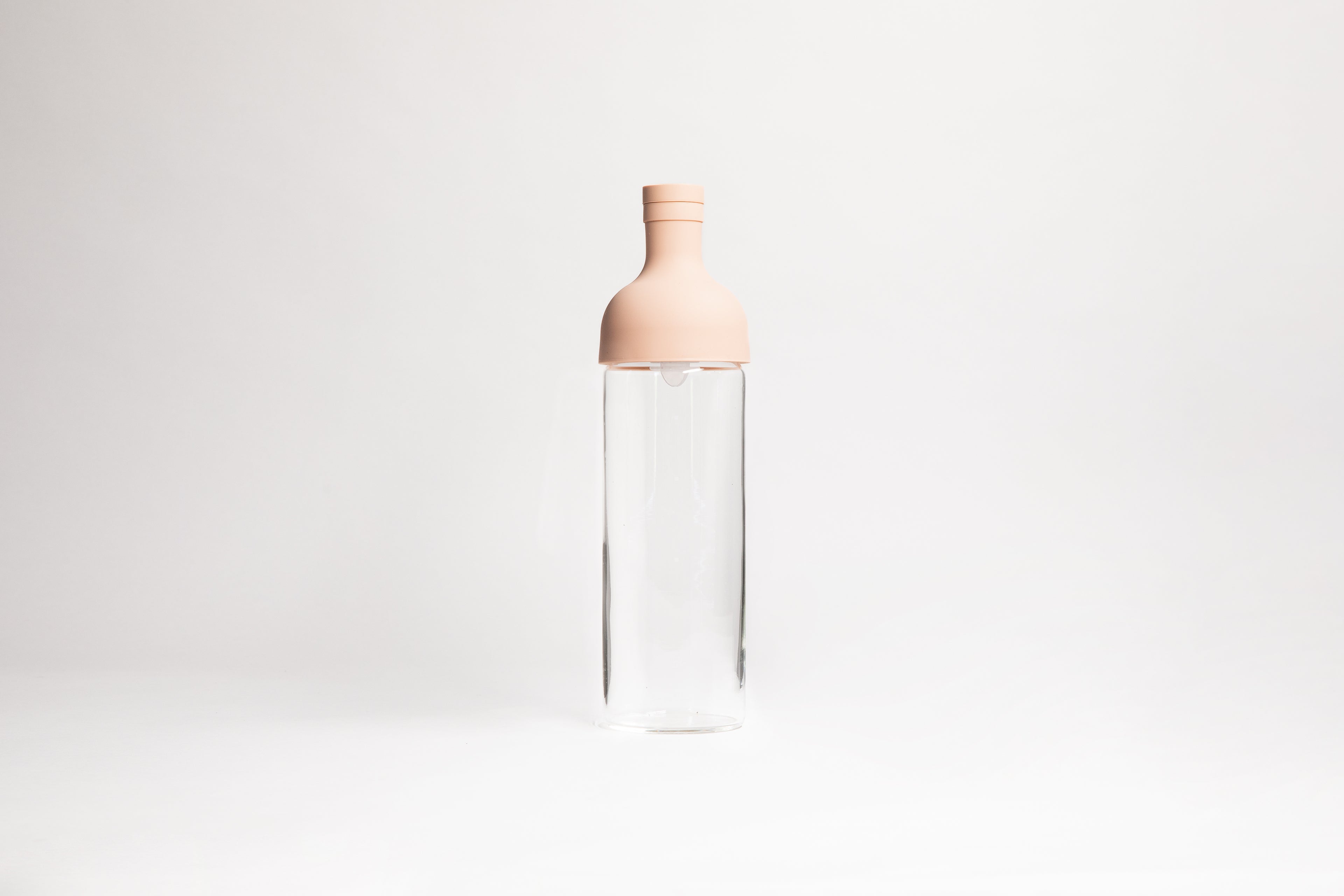 Tall glass container with light pink rubber wine bottle shaped top on an white backdrop.