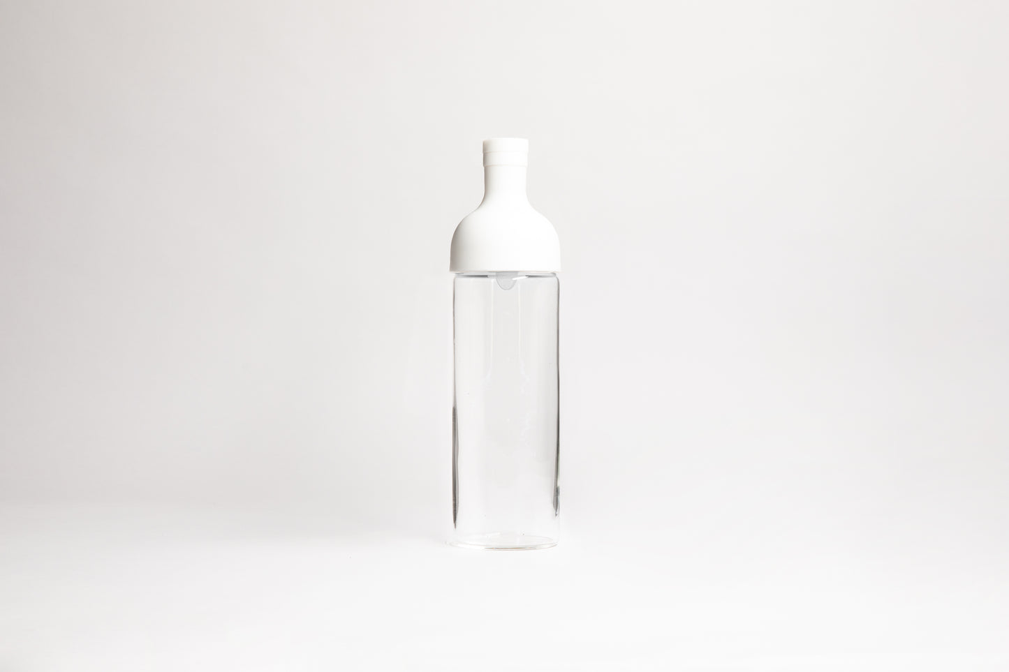 Tall glass container with white rubber wine bottle shaped top on an white backdrop.