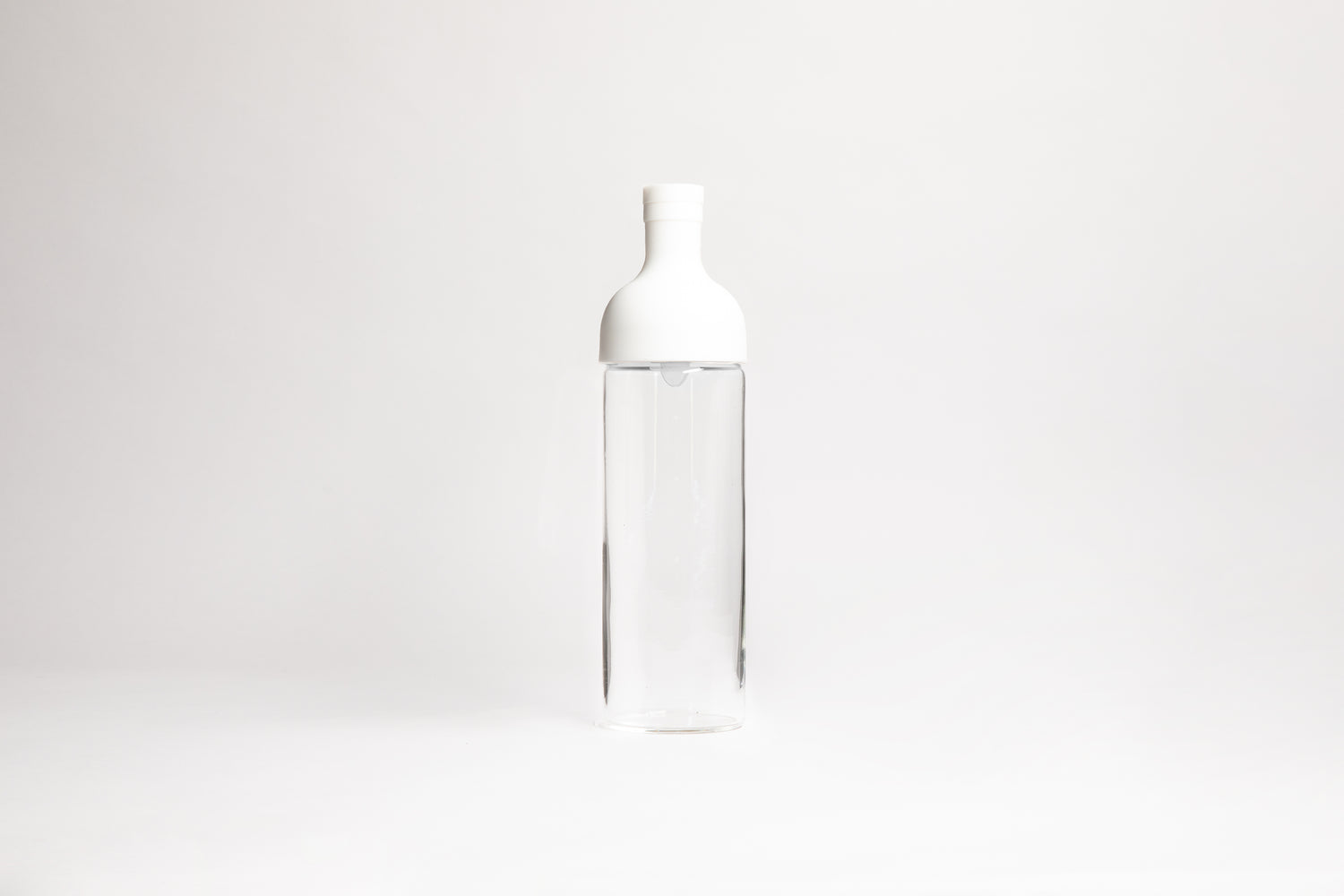 Tall glass container with white rubber wine bottle shaped top on an white backdrop.
