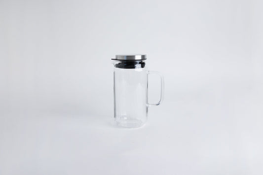 Clear glass pitcher with glass handle with metal lid and black gasket. seton a white background