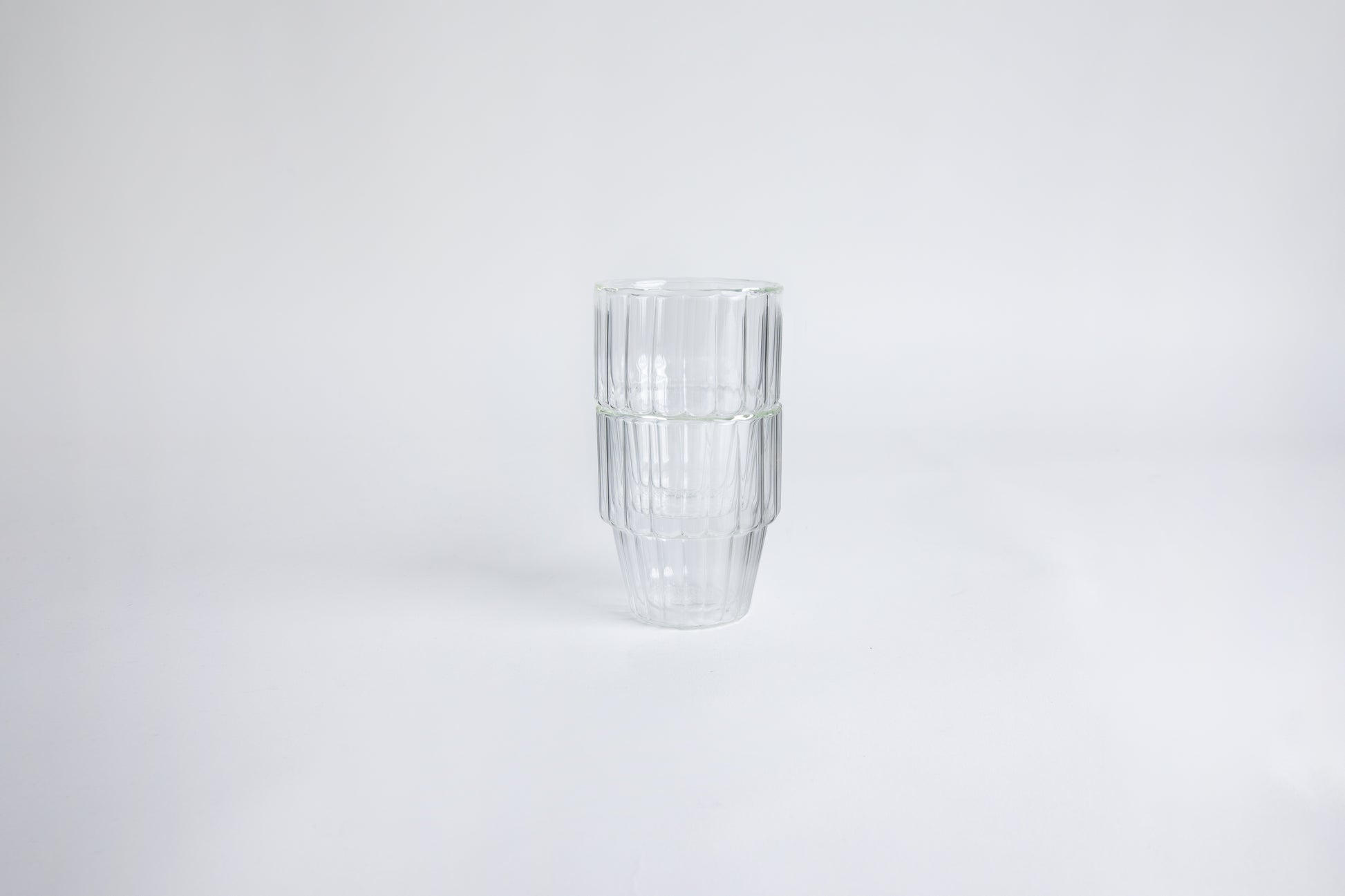 2 ribbed glass cups stacked on top of each other. set on a white background.