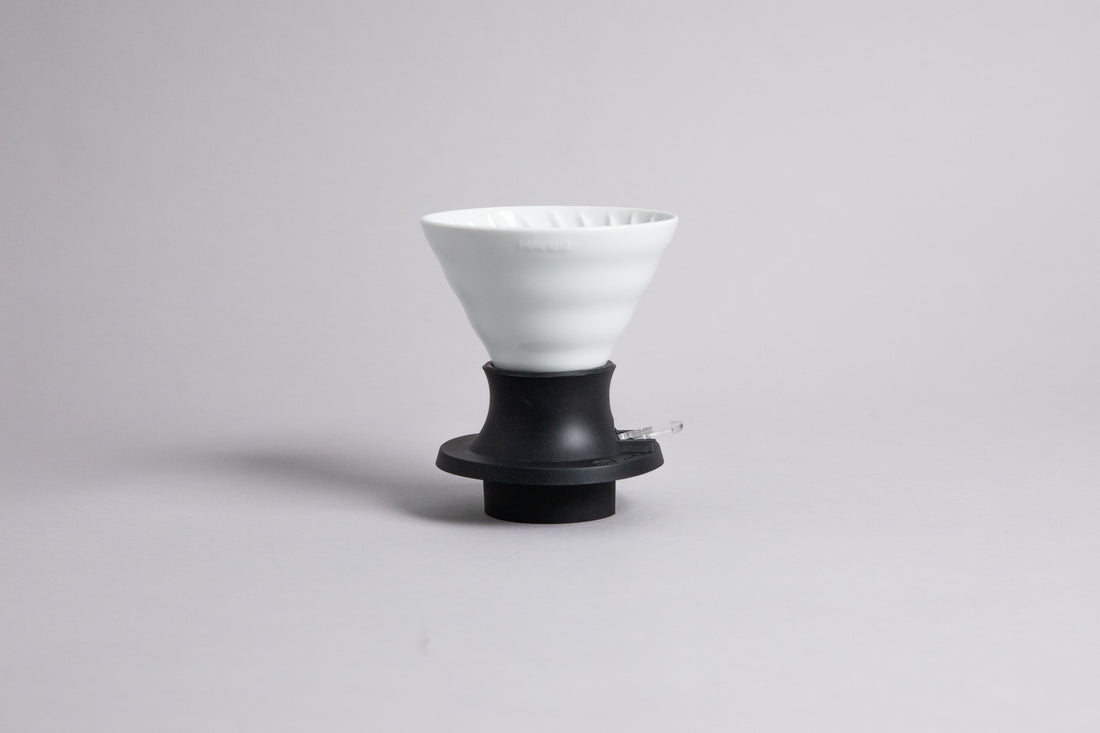 Cone-shaped white ceramic dripper seated in a black plastic silicone base with clear plastic push switch on a gray background.
