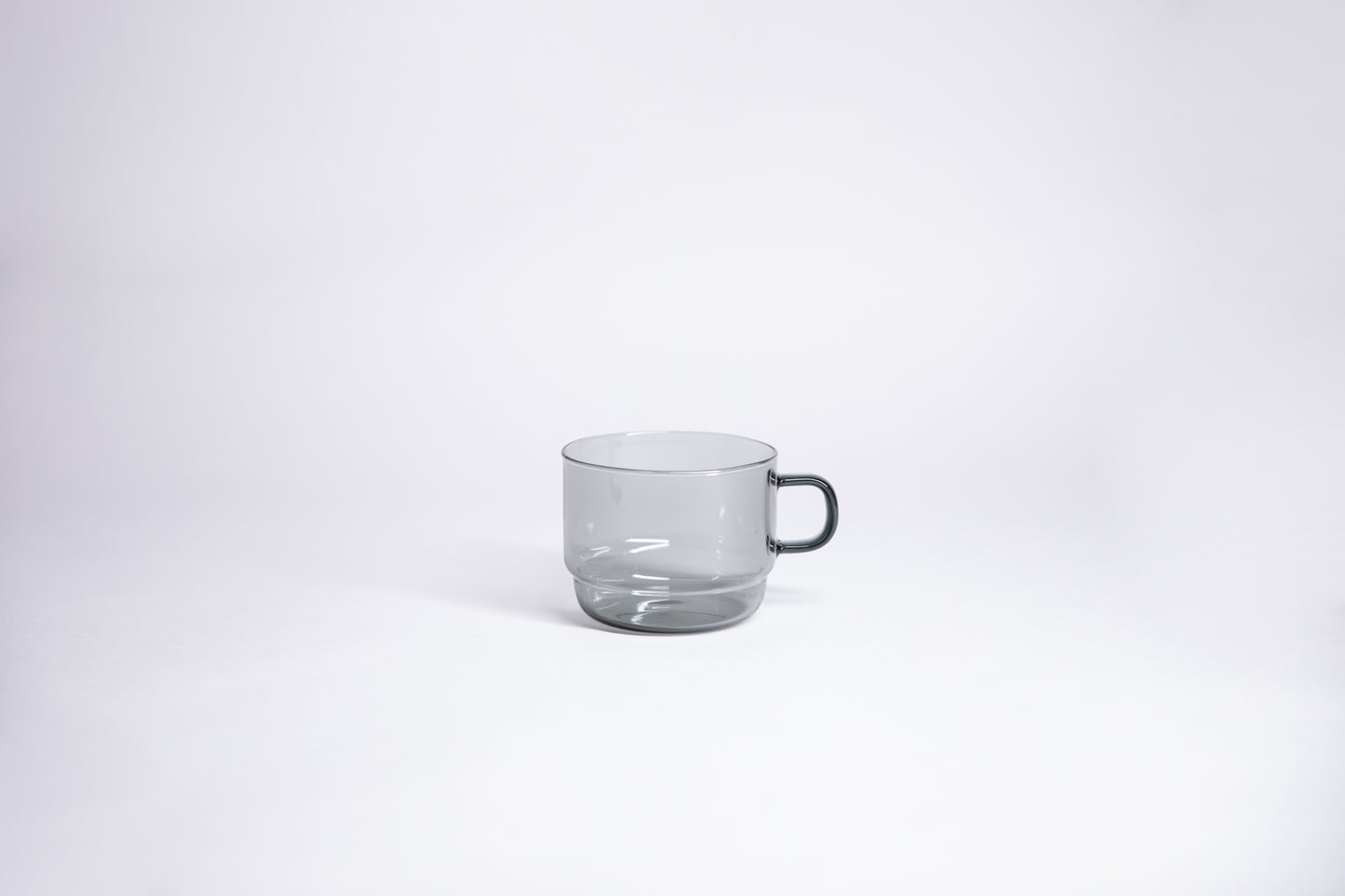Small transparent gray glass mug with handle. set on white background