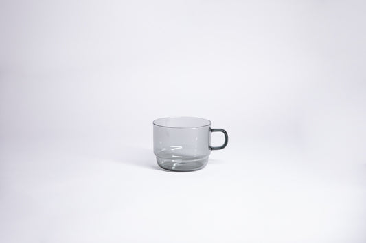 Small transparent gray glass mug with handle. set on white background