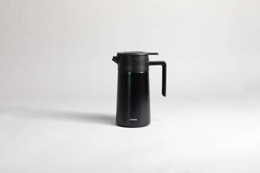 Black cylincial pot with an black polypropylene spout, handle and lid. Set on a light gray background.