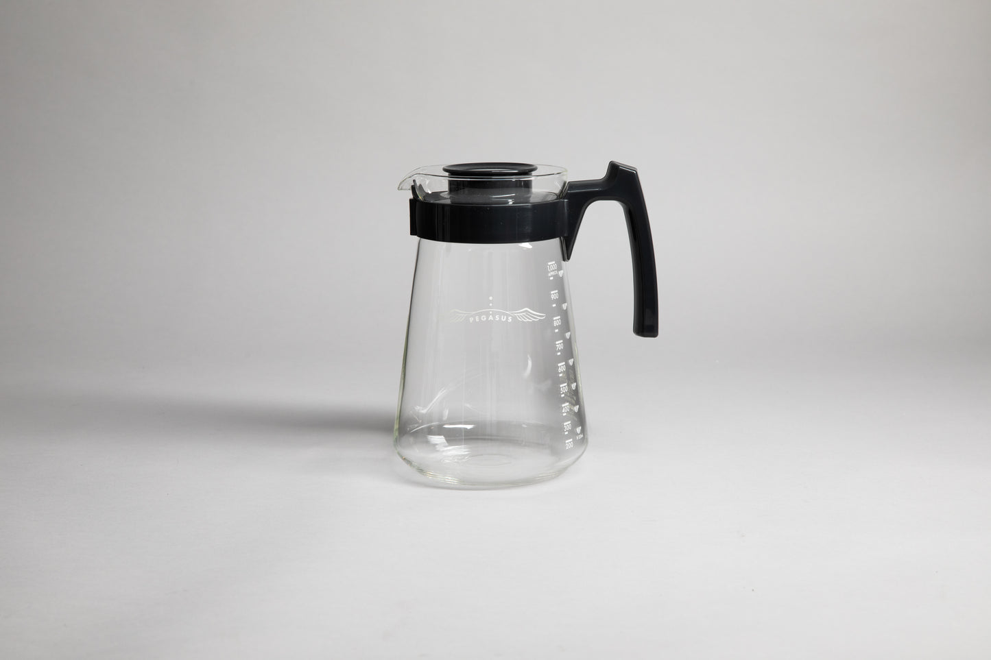 Glass coffee server with white text and level markings with black hard plastic handle and lid on a light grey background.