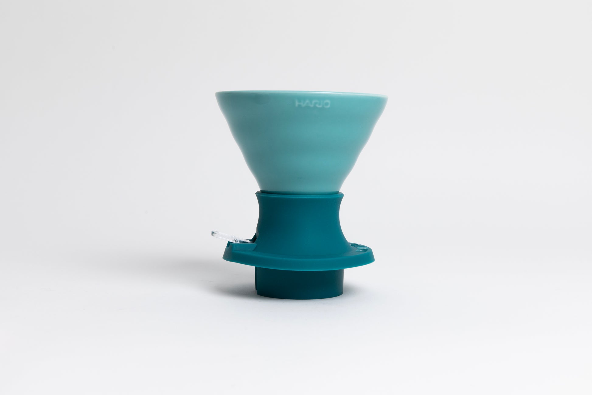 Cone-shaped turquoise ceramic dripper seated in a dark turquoise silicone base with clear plastic push switch on a white background.