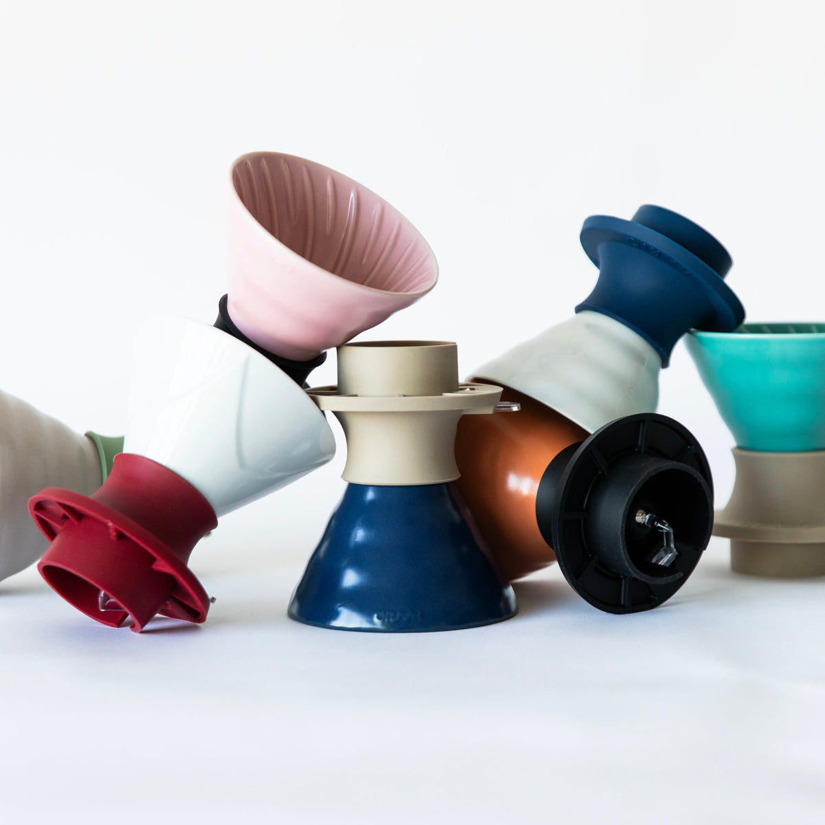 A colorful assortment of V60 ceramic cone coffee drippers with various silicone bases, arranged in a pile on a white background.