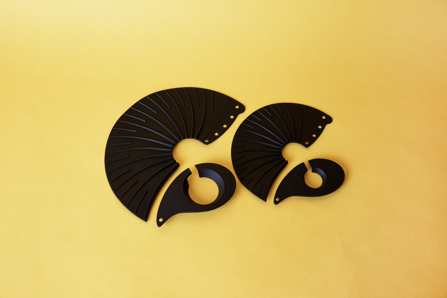 Photo shows size comparison large and small flattened out cone drippers; arch shaped silicone with ribs and 4 punched out holes and two C shaped plastic base. Set on yellow background.