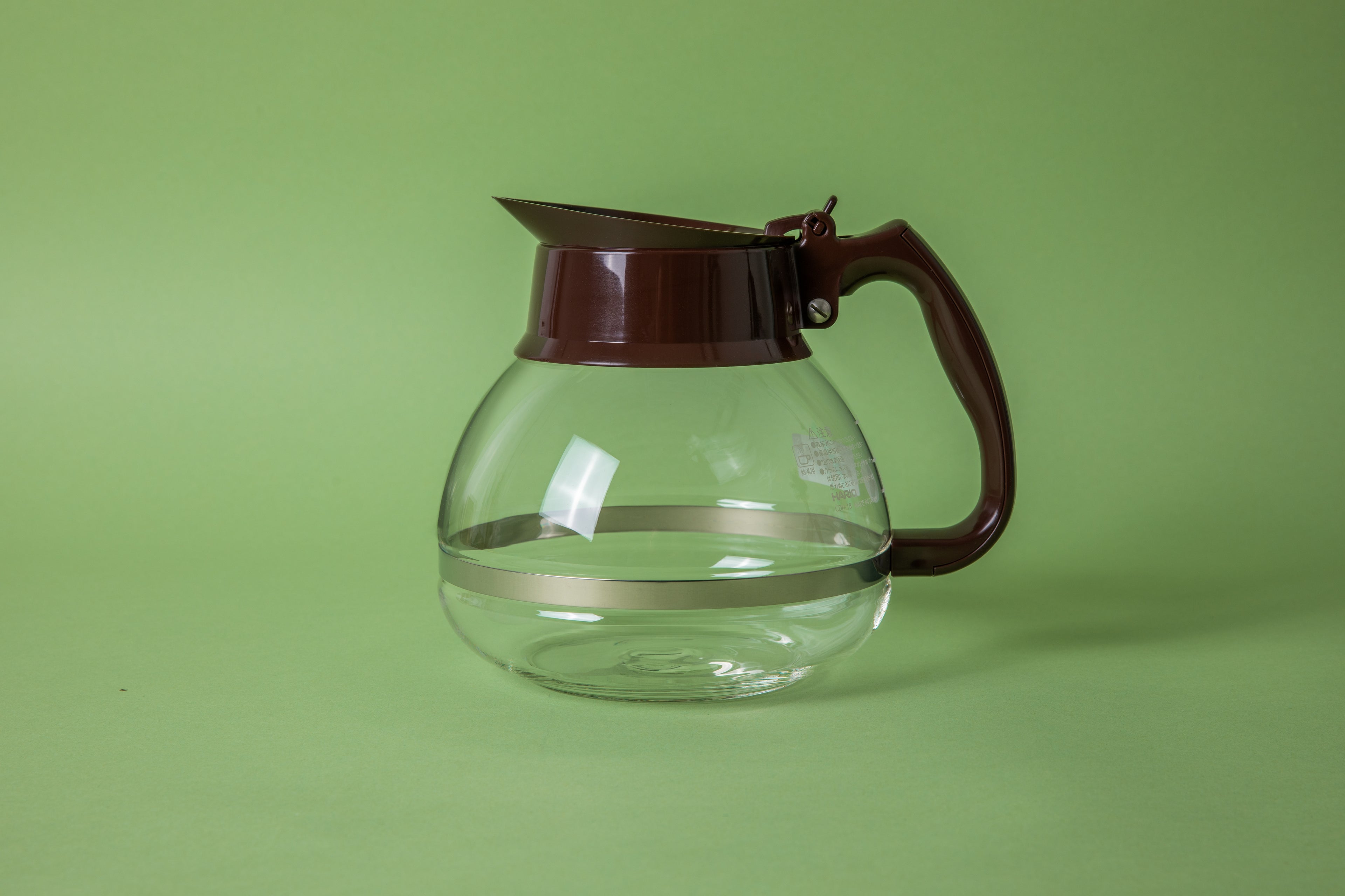 Vintage glass round decanter with brown plastic handle and fluted spout. With thin metal collar around the glass. Set on a green background