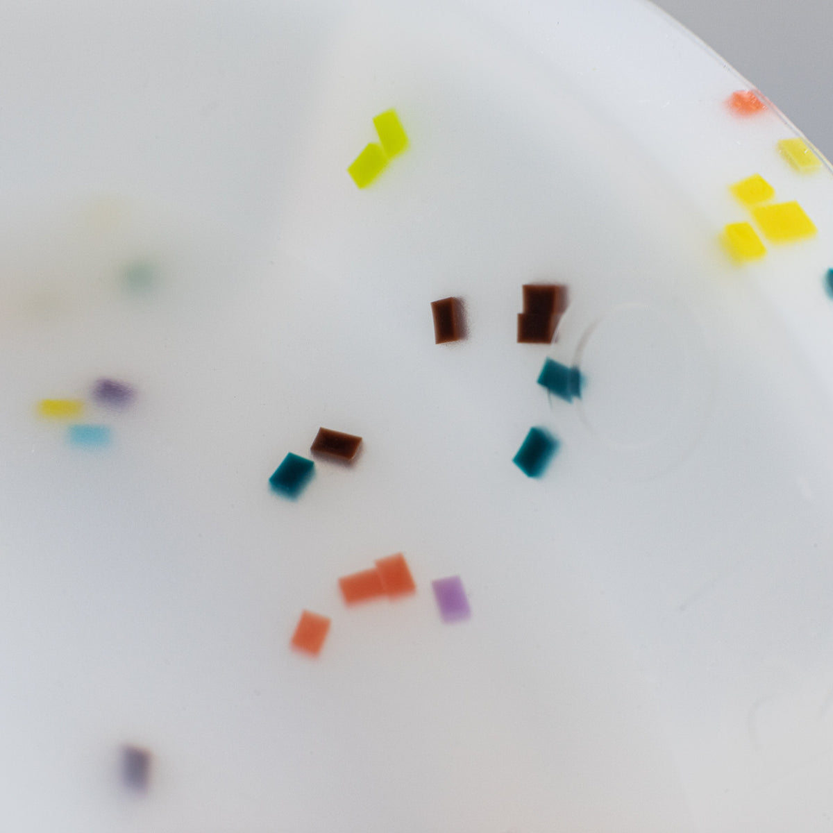 close up on the speckles on the white base. speckles are in the color: orange, purple, dark teal, yellow and lime green.