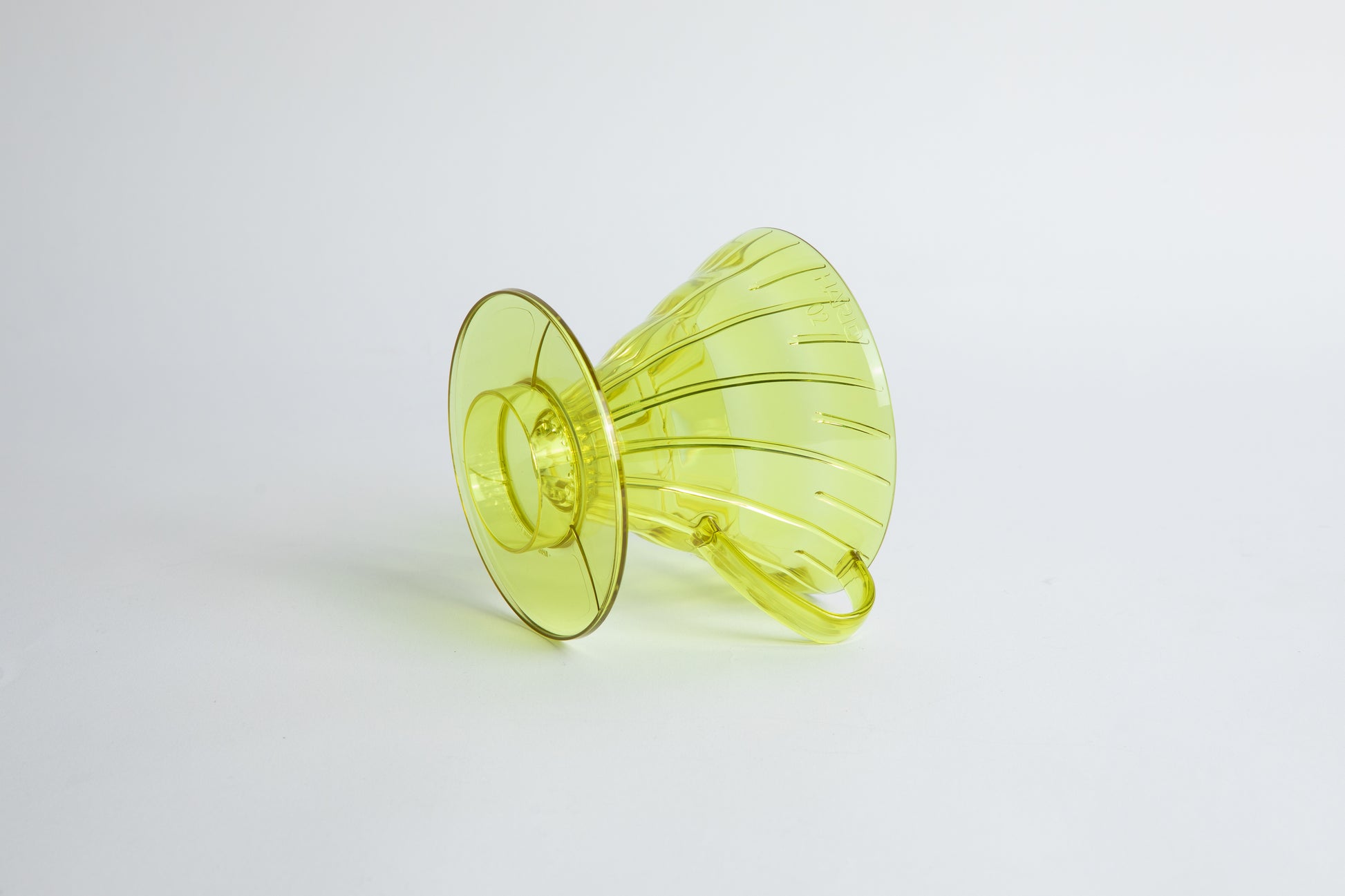 set on it's side the Size 02 Plastic V60 Dripper in the color transparent Chartreuse (Aurora) with a cylindrical base and curved handle. Set on a white background
