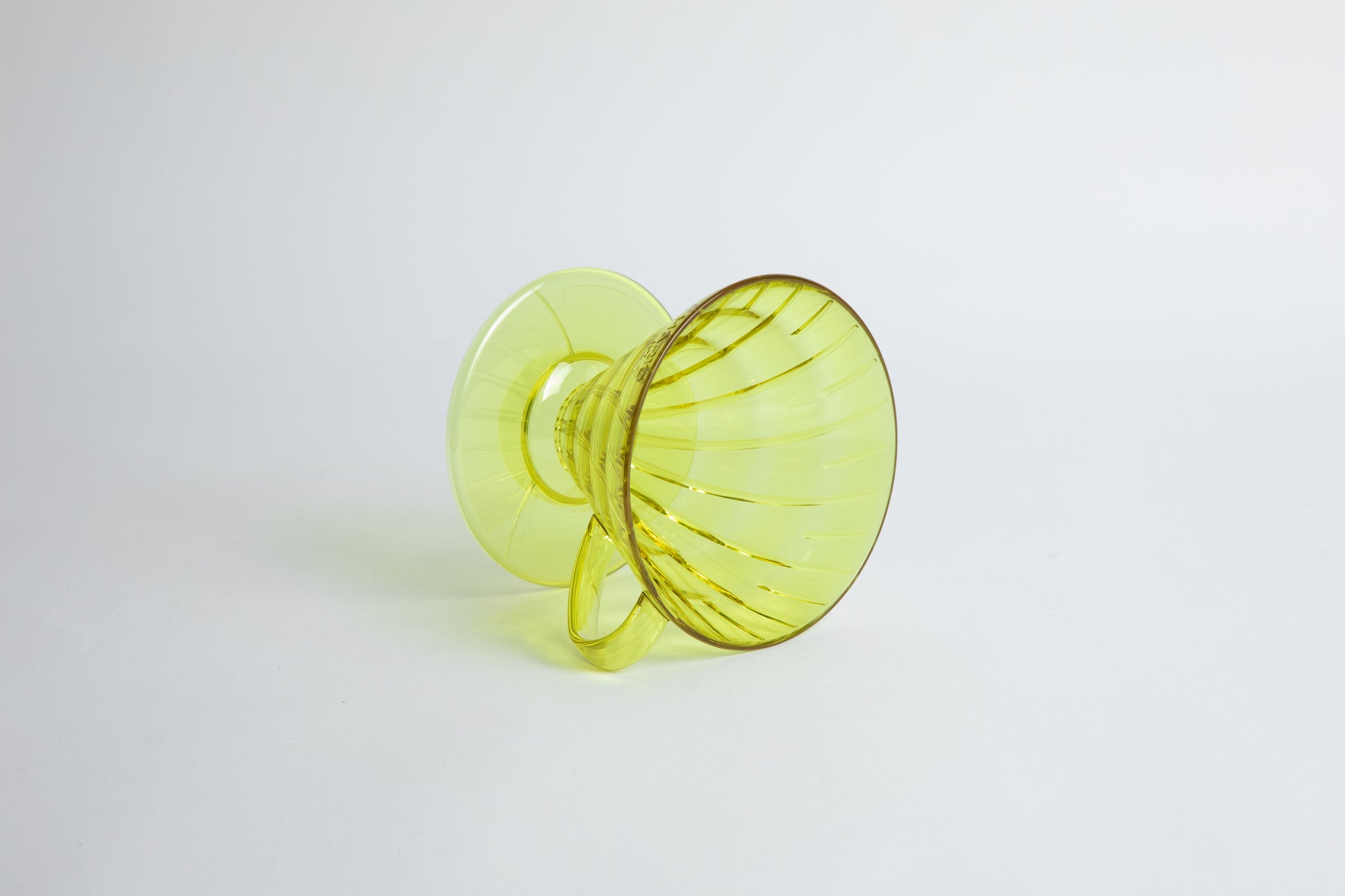 set on it's side the Size 02 Plastic V60 Dripper in the color transparent Chartreuse (Aurora) with a cylindrical base and curved handle. Set on a white background