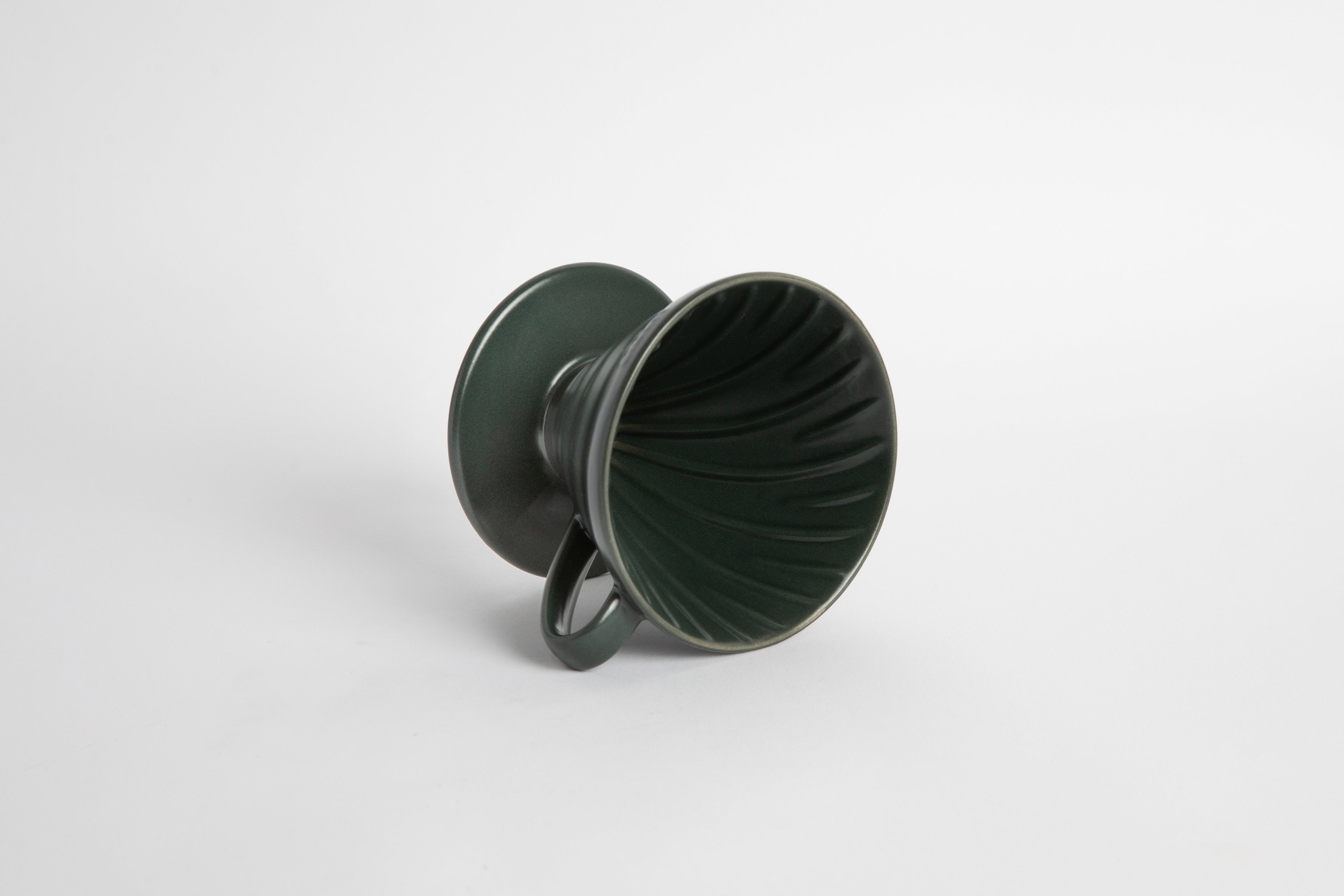 Dark green colored 60 degree cone shaped ceramic coffee dripper with handle and round base. Spiral ribbed on the inside cone. Set on white background