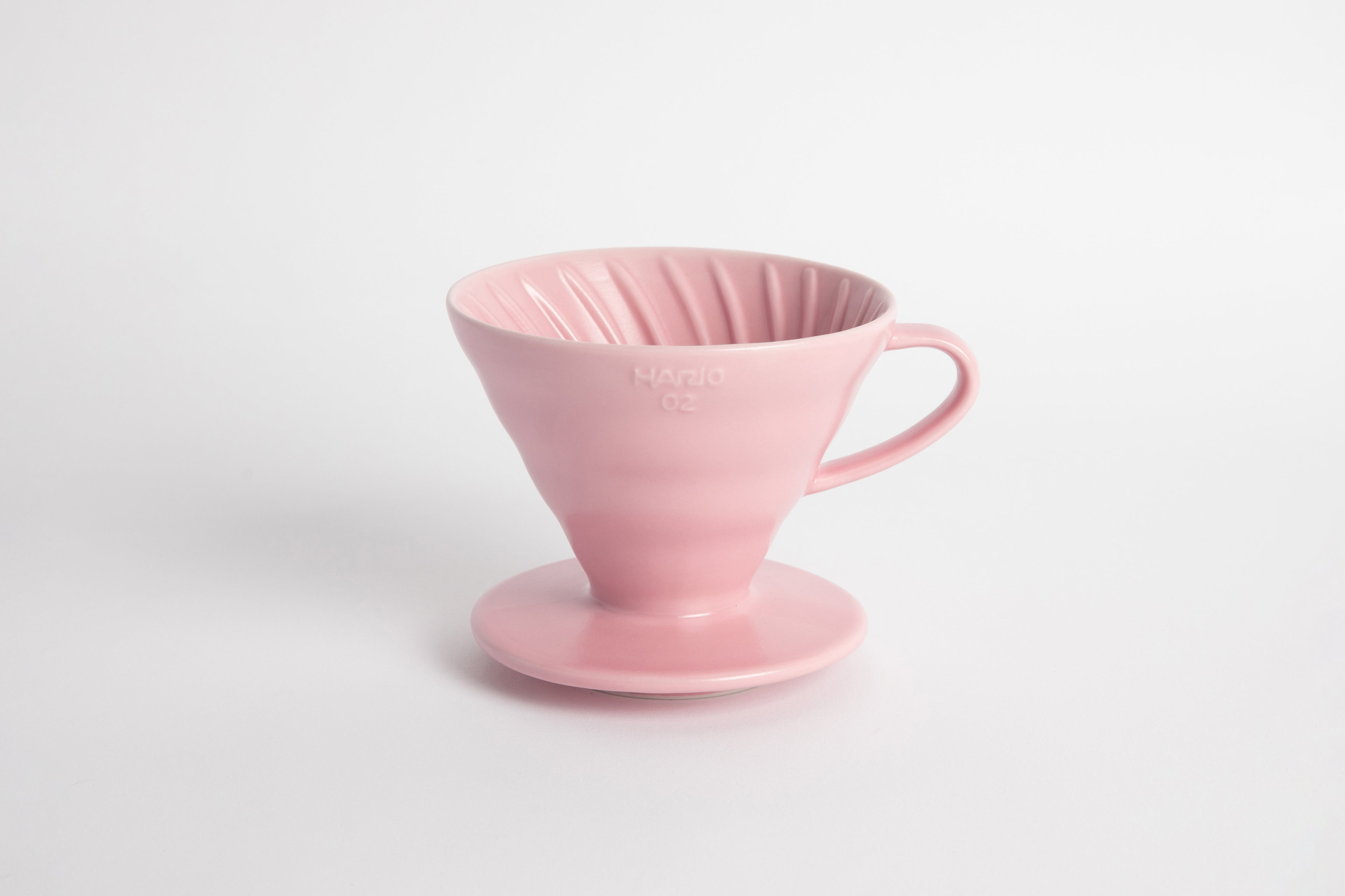 Pink colored 60 degree cone shaped ceramic coffee dripper with handle and round base. Spiral ribbed on the inside cone. Set on white background