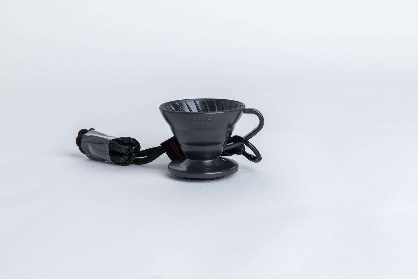 black cone shaped plastic coffee dripper cup with handle and round base. with a black rope tied on the handle Set on white background