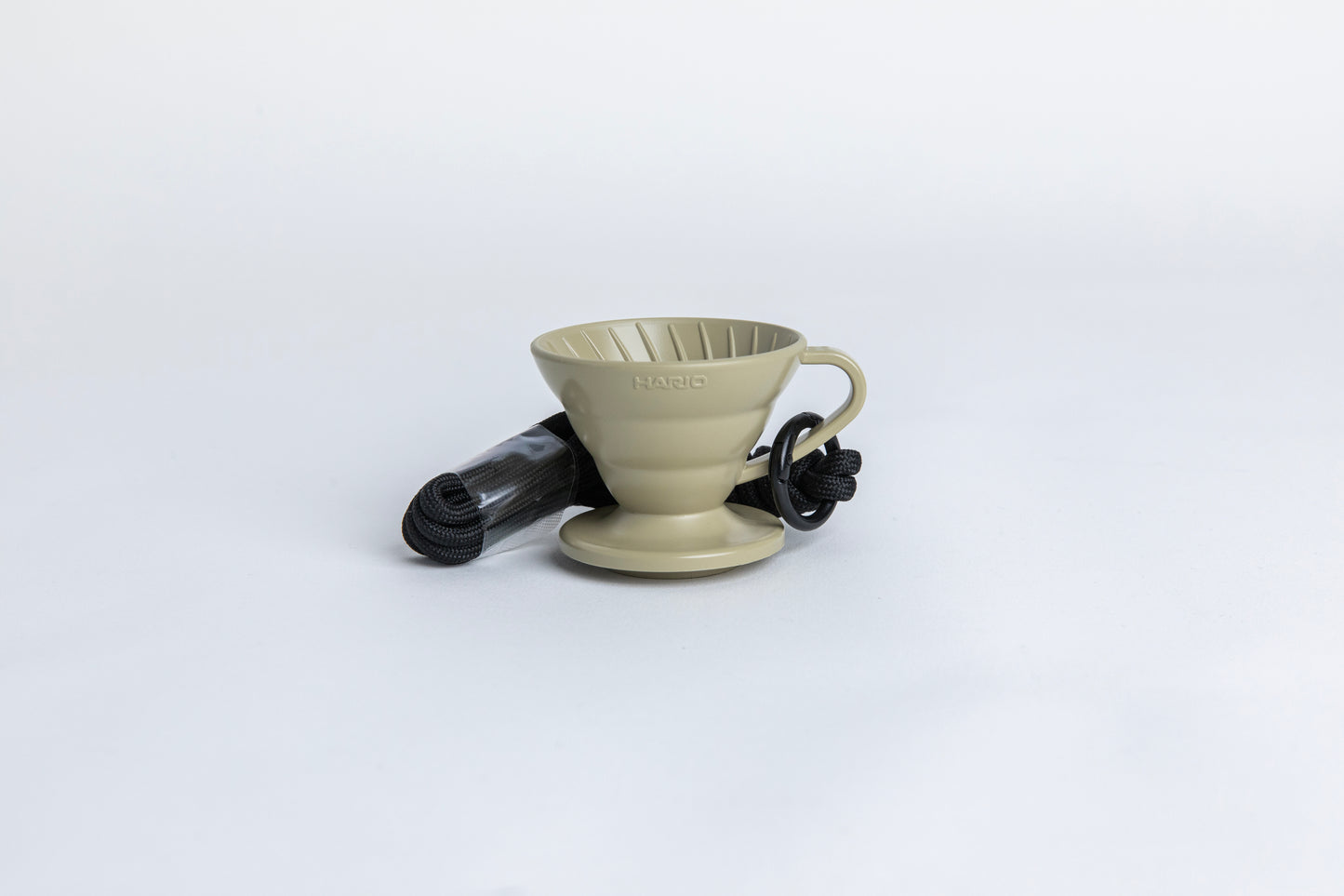 khaki cone shaped plastic coffee dripper cup with handle and round base. with a black rope tied on the handle Set on white background
