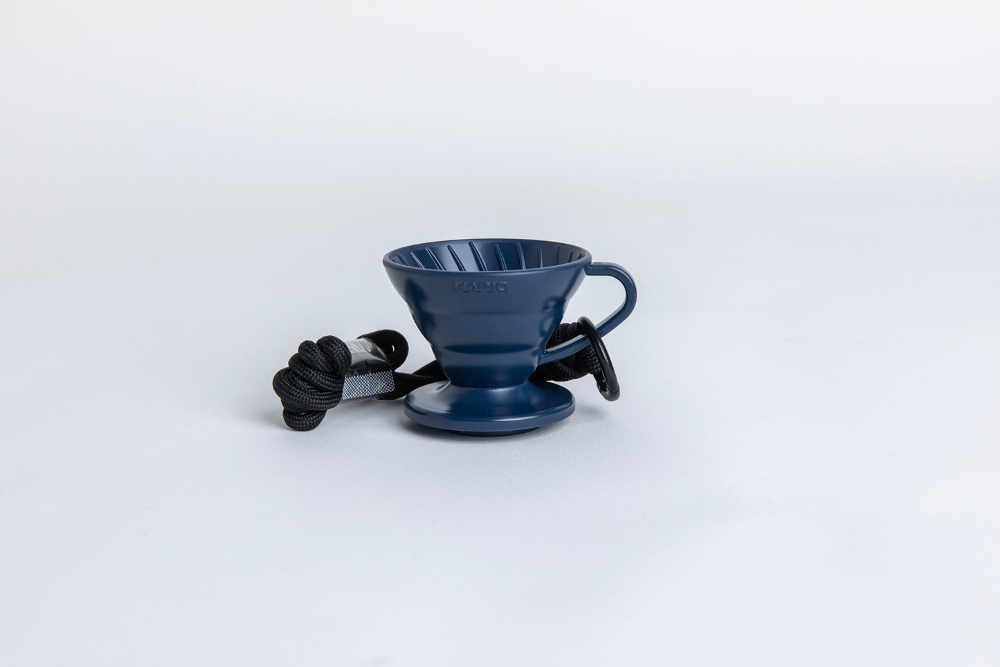 navy blue cone shaped plastic coffee dripper cup with handle and round base. with a black rope tied on the handle Set on white background