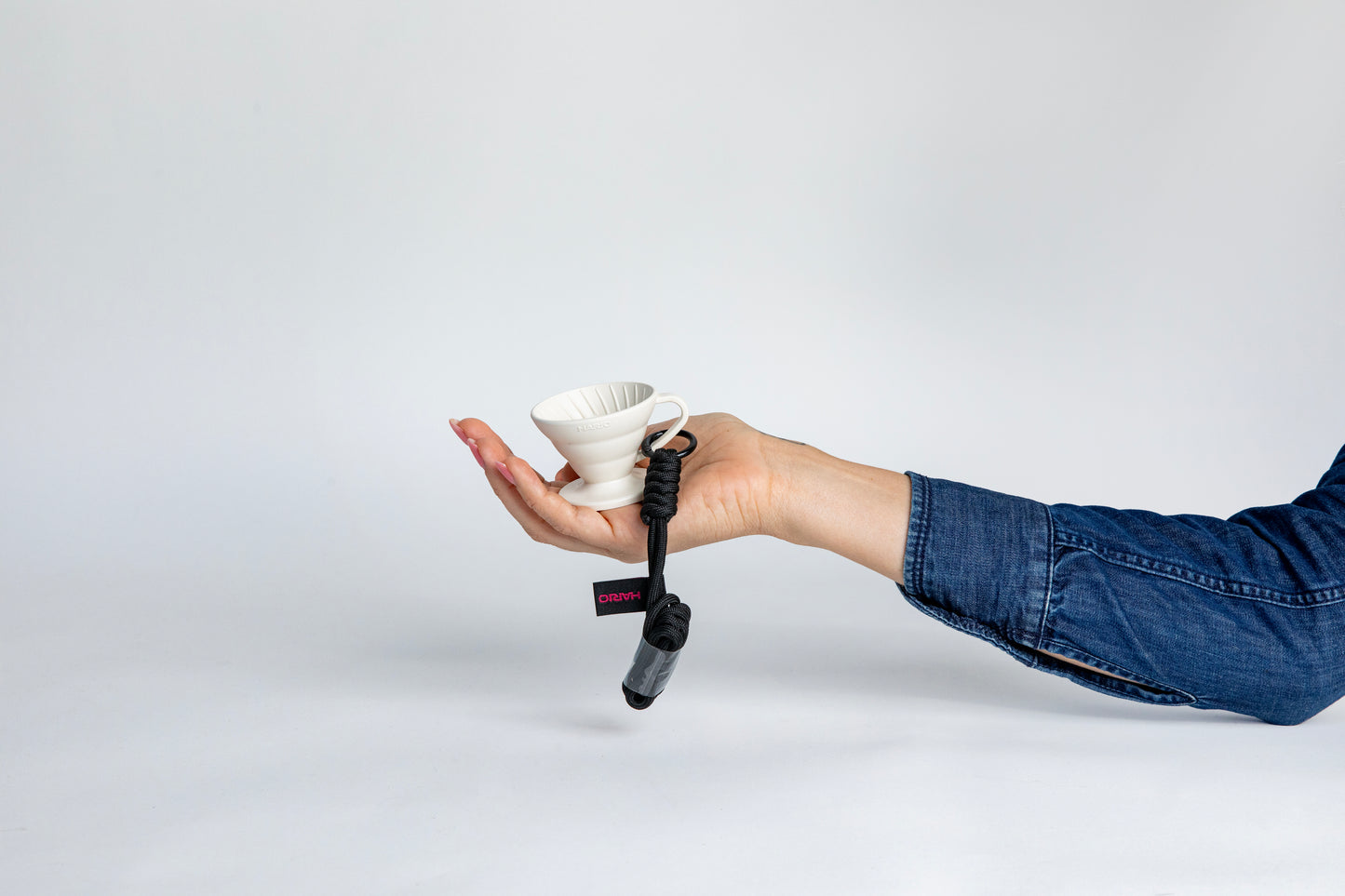 hand holding the white black cone shaped ceramic coffee dripper cup with handle and round base. with a brown rope tied on the handle, showcasing the size of the small cup can fit in the palm of a hand. Set on white background