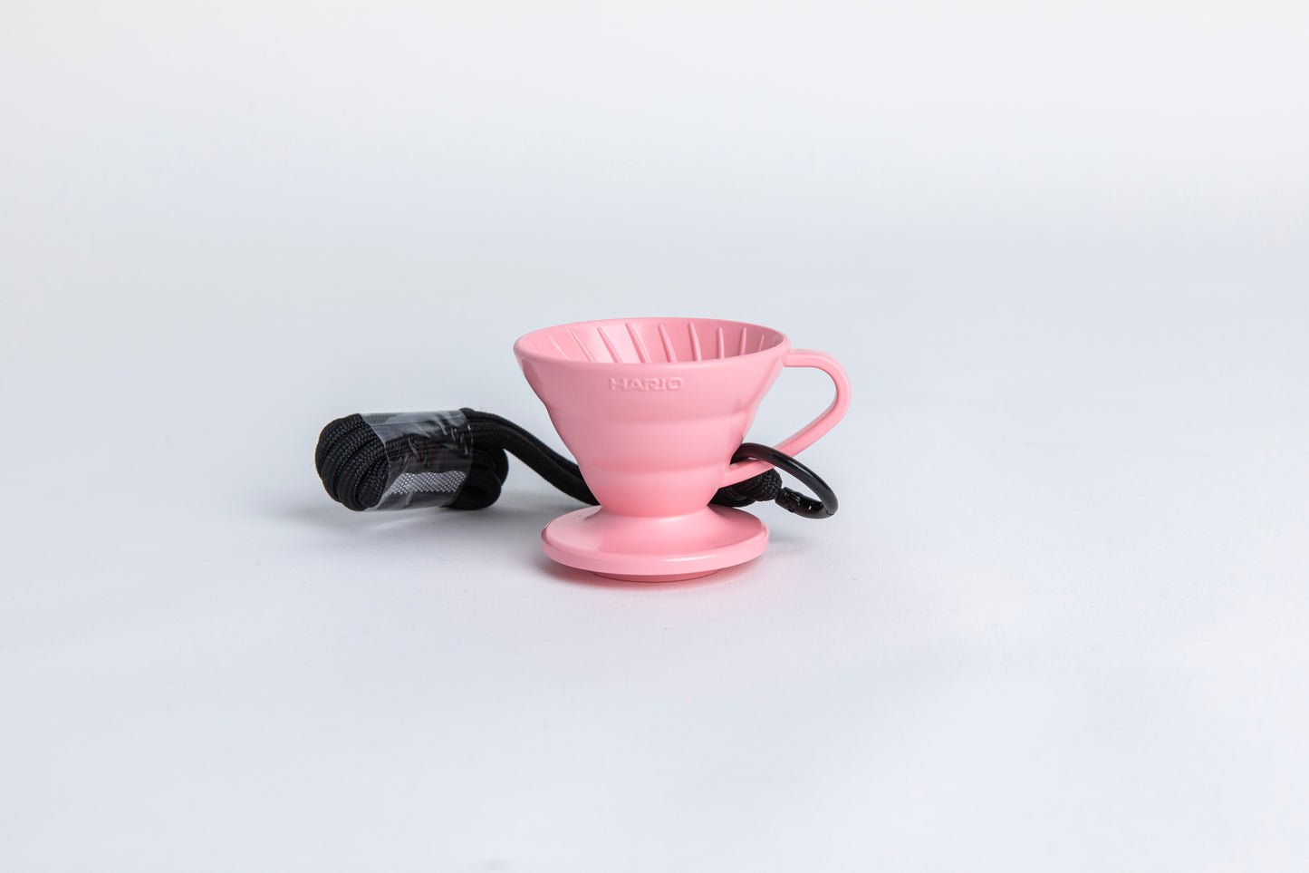 pink cone shaped plastic coffee dripper cup with handle and round base. with a black rope tied on the handle Set on white background