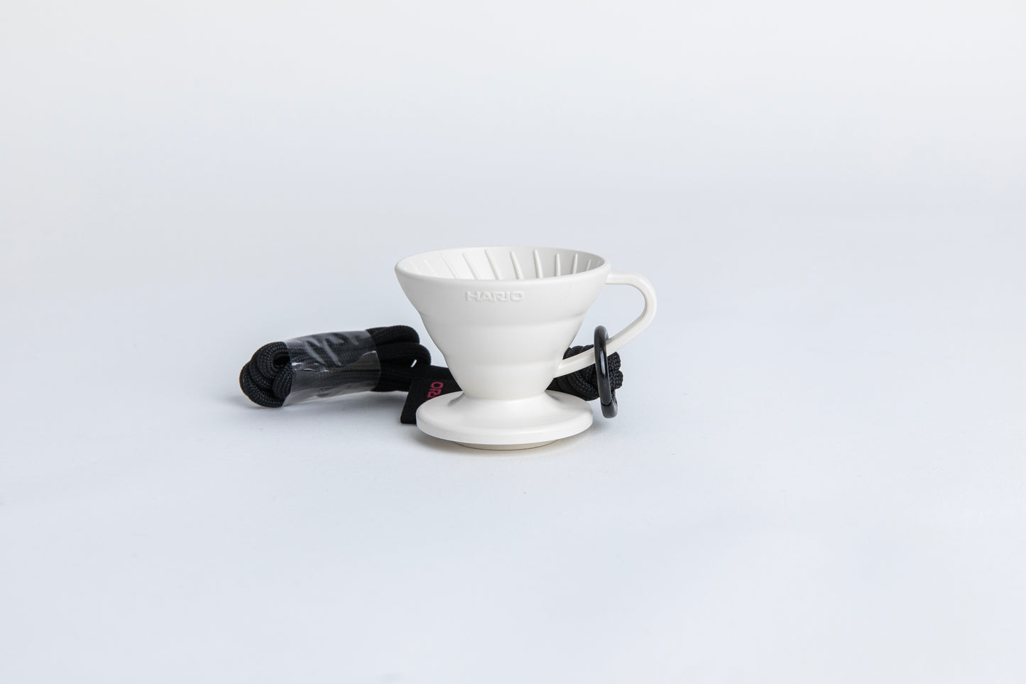 white cone shaped plastic coffee dripper cup with handle and round base. with a black rope tied on the handle Set on white background