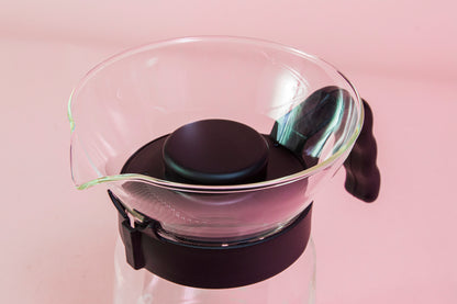 Close up of spout and lid on a tall glass coffee decanter with black plastic handle with a frosted plastic insert and black plastic cone dripper on top with black plastic server lid.
