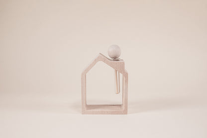 Wooden house frame with wooden stick shaped like a popsicle inside a glass vile on a light brown background.