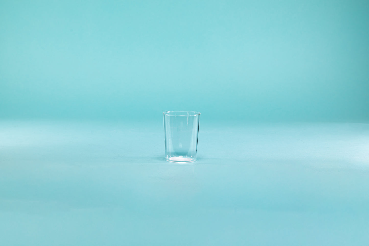 Clear thin walled shot glass on blue background.