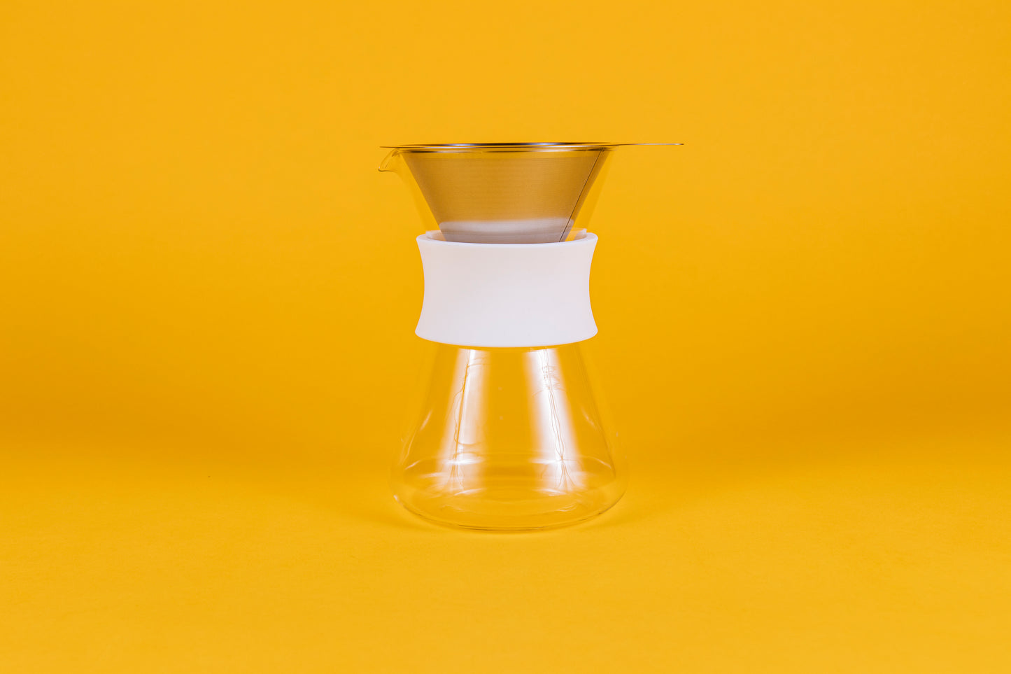 Clear glass server with white silicone collar and stainless steel mesh filter against a yellow background.