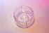 Clear plastic ring with interior smaller ring and holes for liquid to drain through. Set on a pink background.