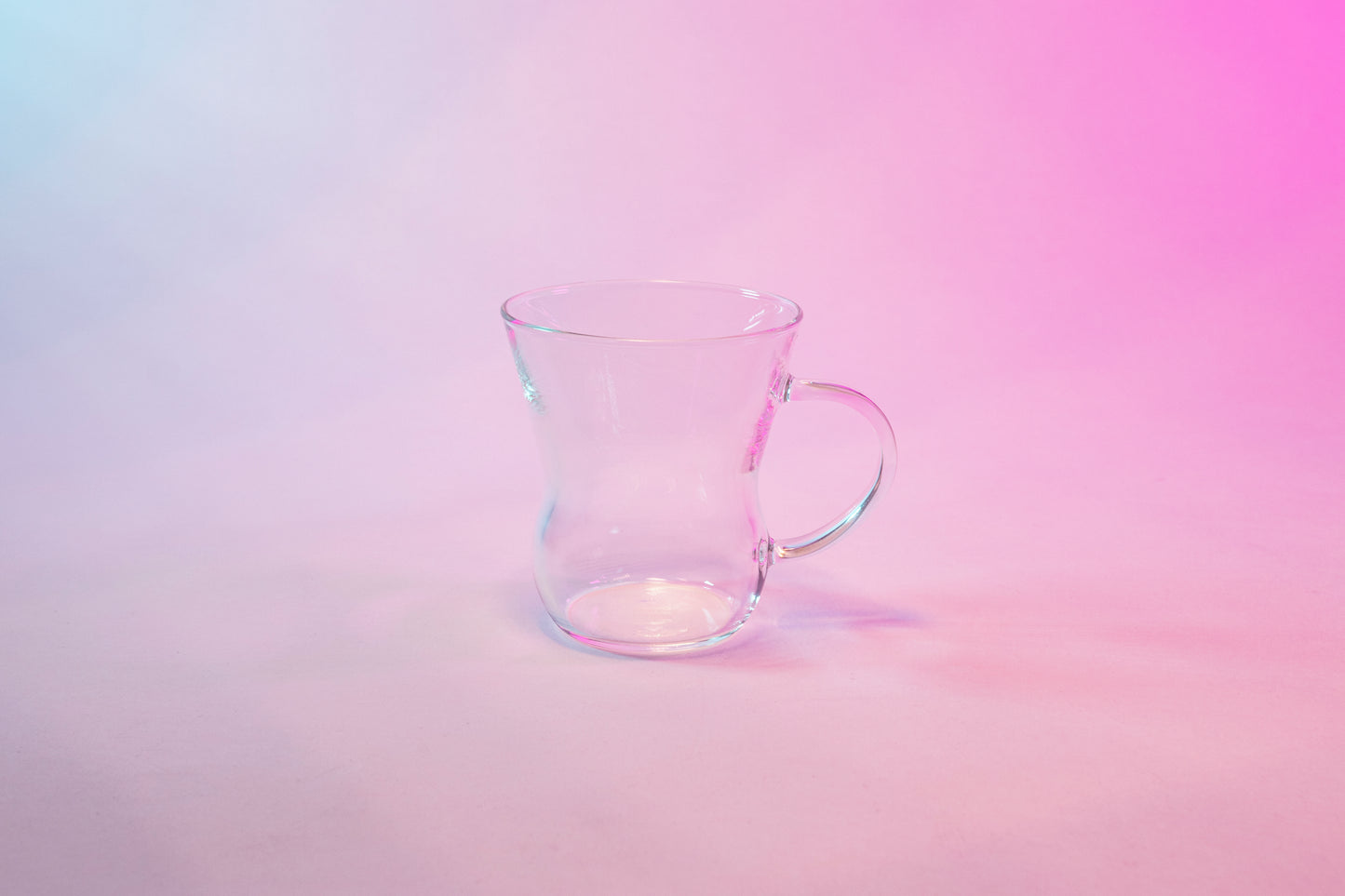 Clear glass tapered mug with full glass handle against a background with blue to violet gradient.
