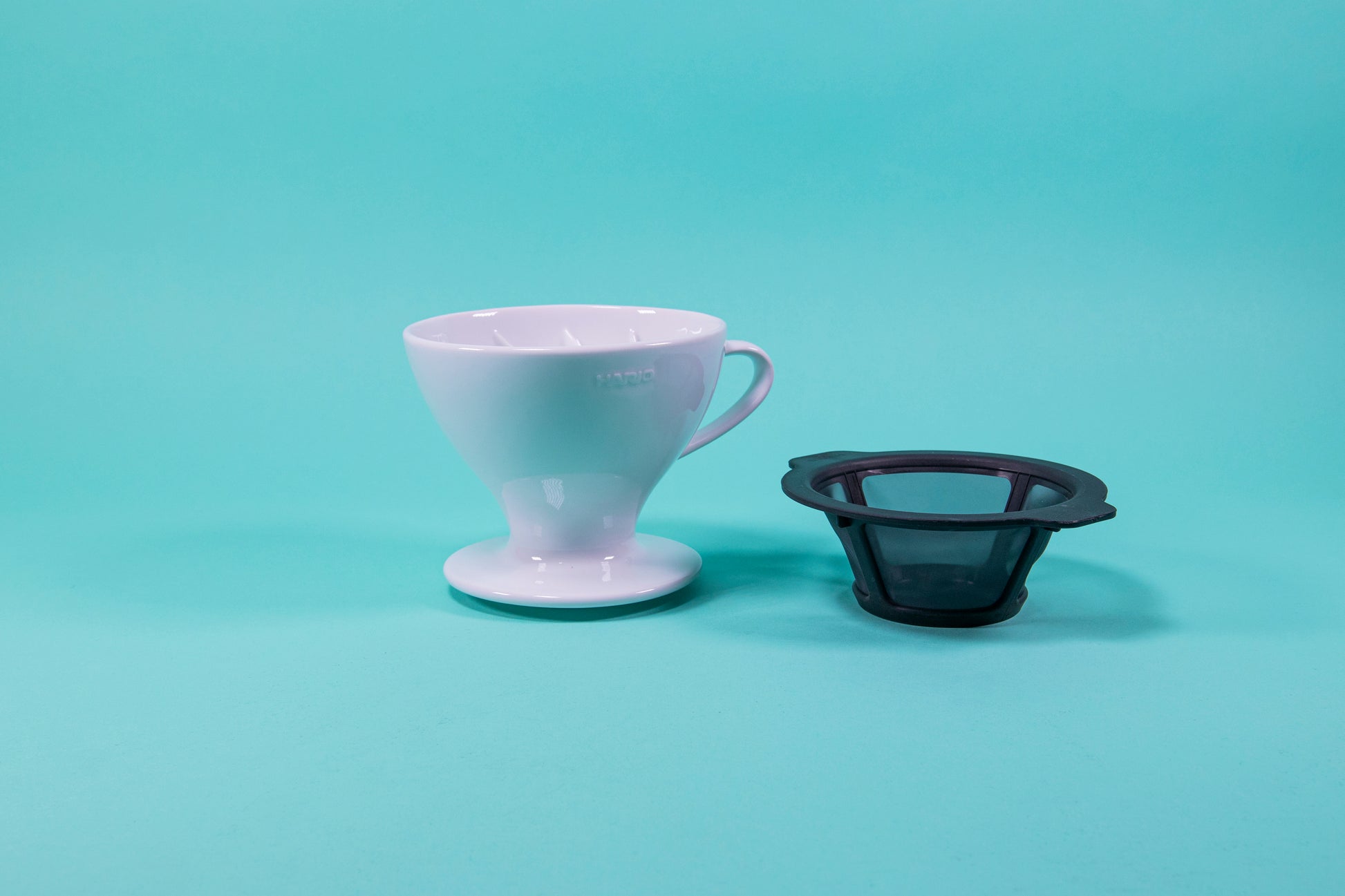 White ceramic cone shaped dripper with ridges inside, rounded eges, and black plastic filter insert seated next to it on a blue background.