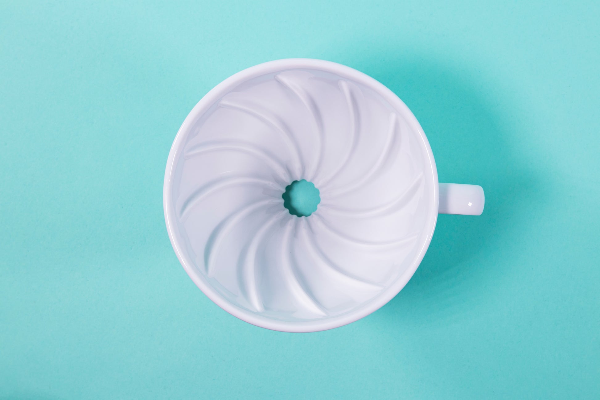 Aerial shot of wavy ridges inside a white ceramic cone shaped dripper on a blue background.