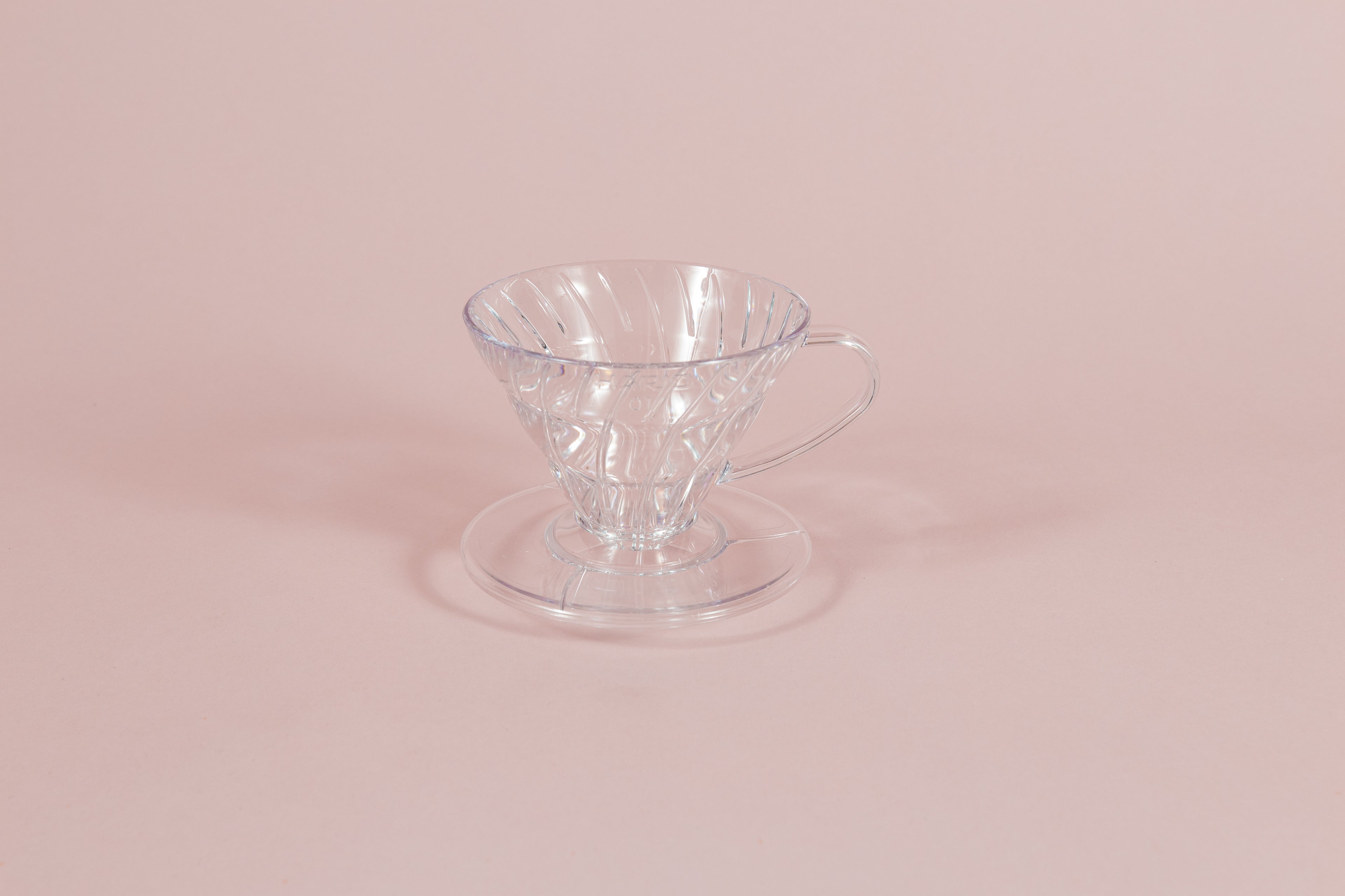 Clear all plastic cone shaped dripper with handle and round base on a pink backdrop.