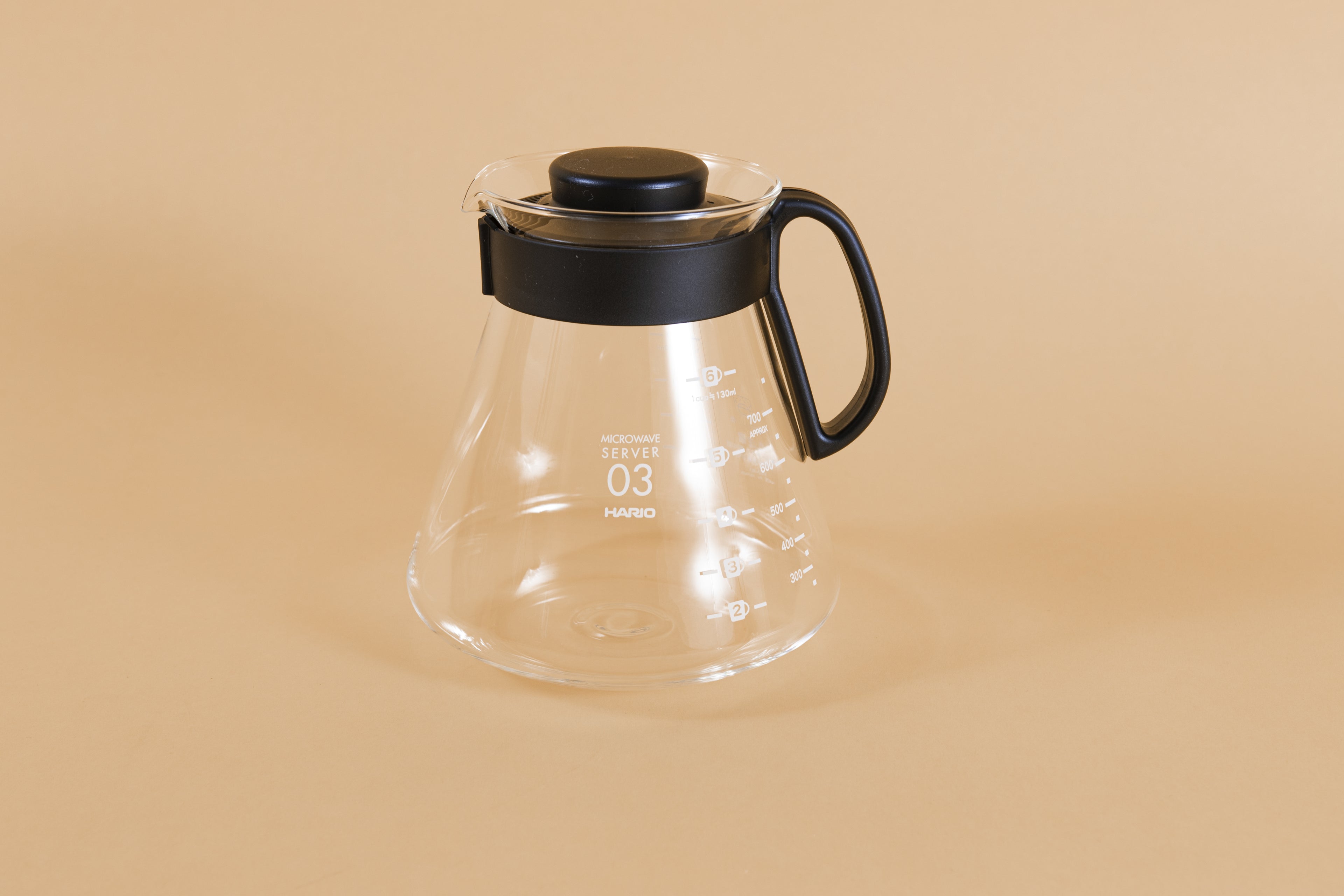 Glass coffee server with white text and level markings with closed black plastic handle and lid on an orange backdrop.