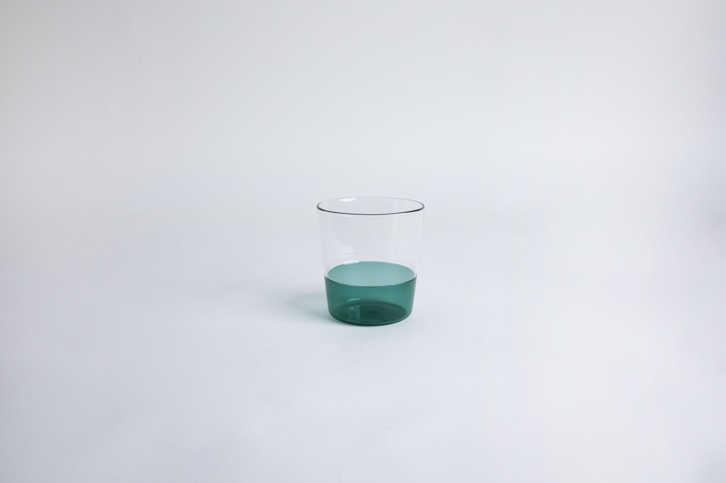 Dual colored clear glass cup, top  half is clear and second half colored teal green set on a white background