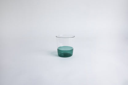 Dual colored clear glass cup, top  half is clear and second half colored teal green set on a white background
