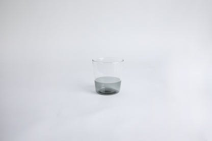 Dual colored clear glass cup, top  half is clear and second half colored gray set on a white background