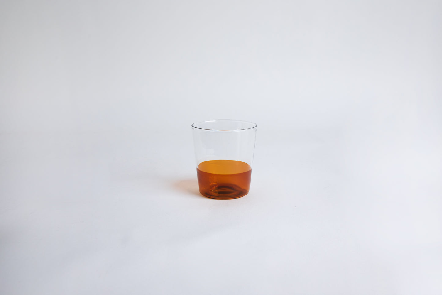 Dual colored clear glass cup, top  half is clear and second half colored amber set on a white background