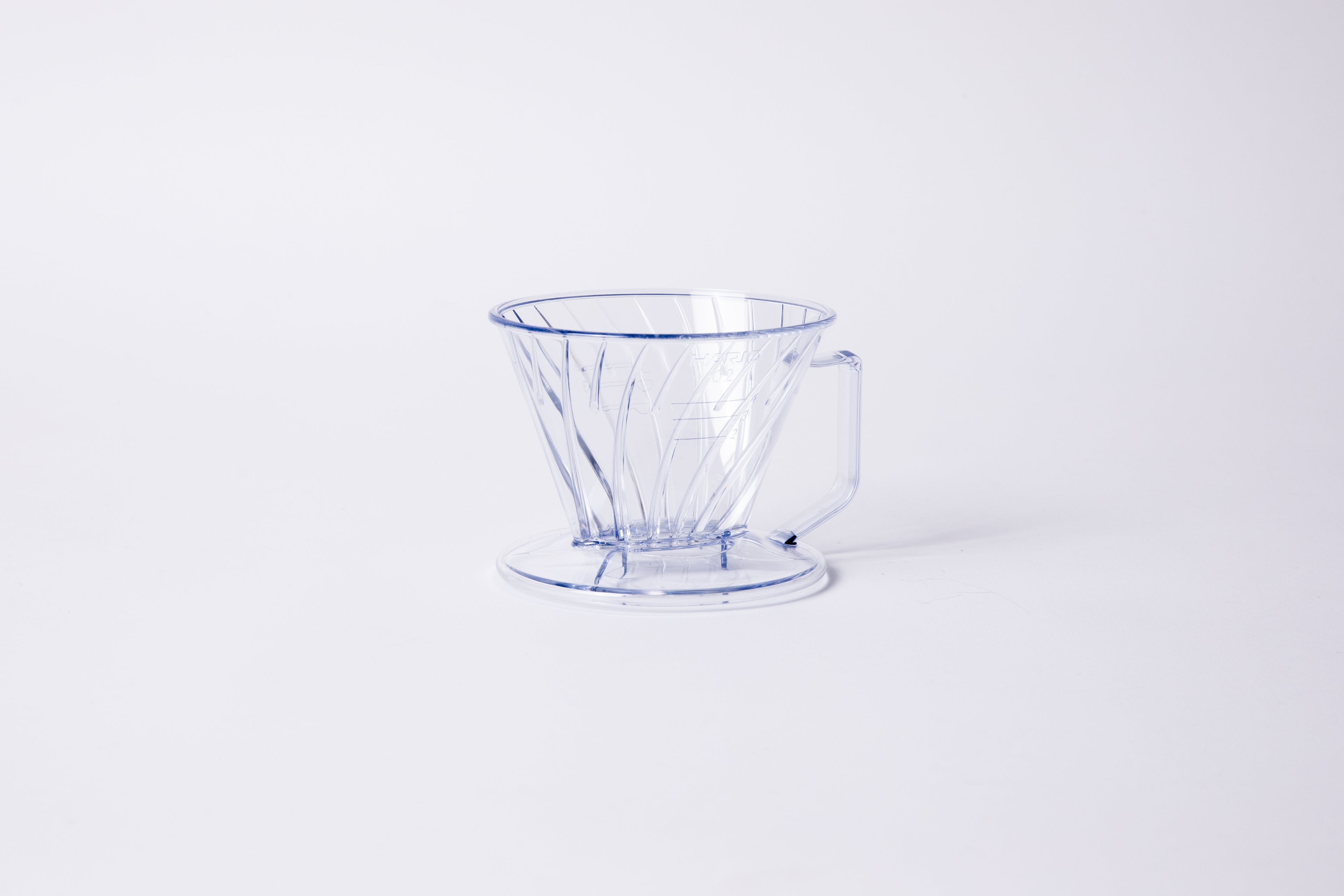 Clear plastic ribbed cone shaped dripper with a flat bottom base and handle. Set on a light gray background