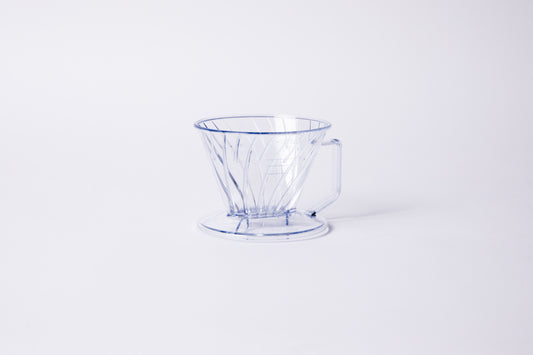 Clear plastic ribbed cone shaped dripper with a flat bottom base and handle. Set on a light gray background