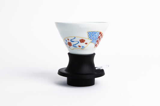 white cone-shaped coffee dripper with fan decotrative design in a black silicone base with clear plastic push switch. set on a white background