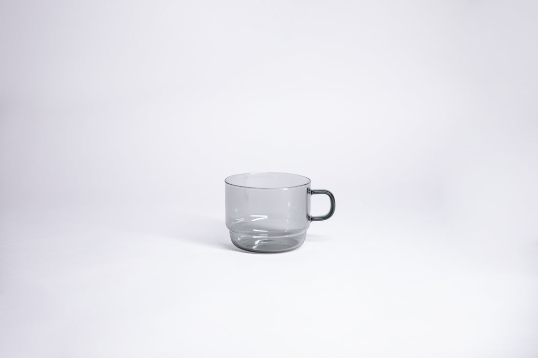 Small transparent gray glass mug with handle. set on white background