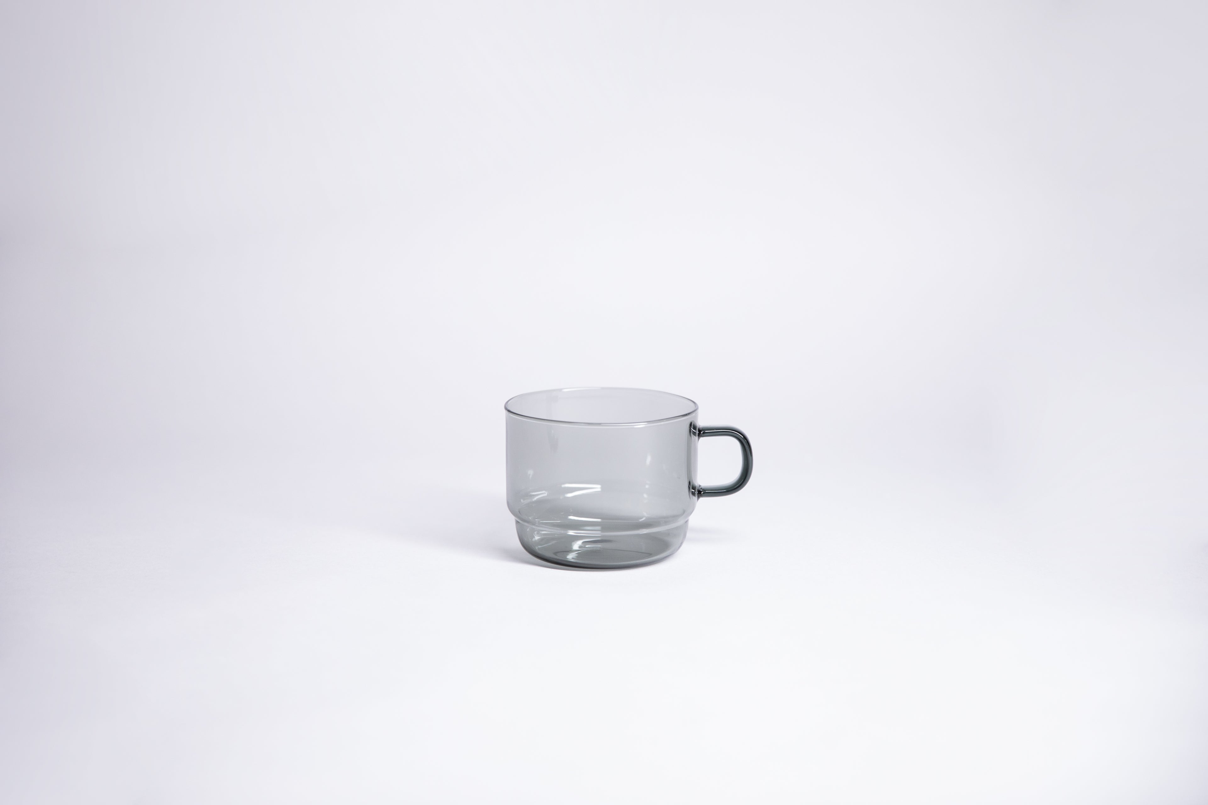 Small transparent gray glass mug with handle. set on white background