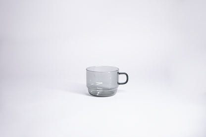 Small transparent gray glass mug with handle. set on white background