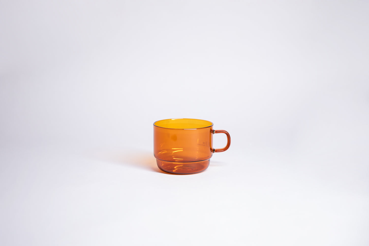 Small transparent amber glass mug with handle. set on white background