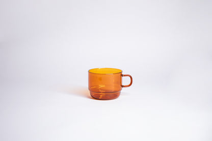 Small transparent amber glass mug with handle. set on white background