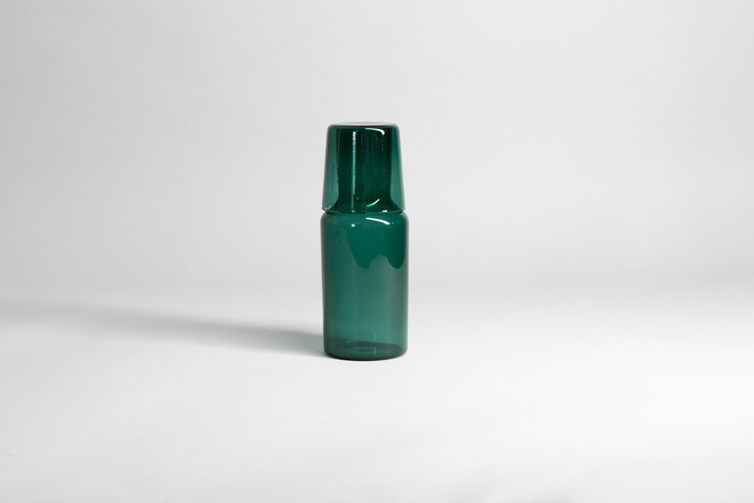 Transparent green carafe with matching glass cup flipped upside down on carafe top of carafe. Set on a light gray background