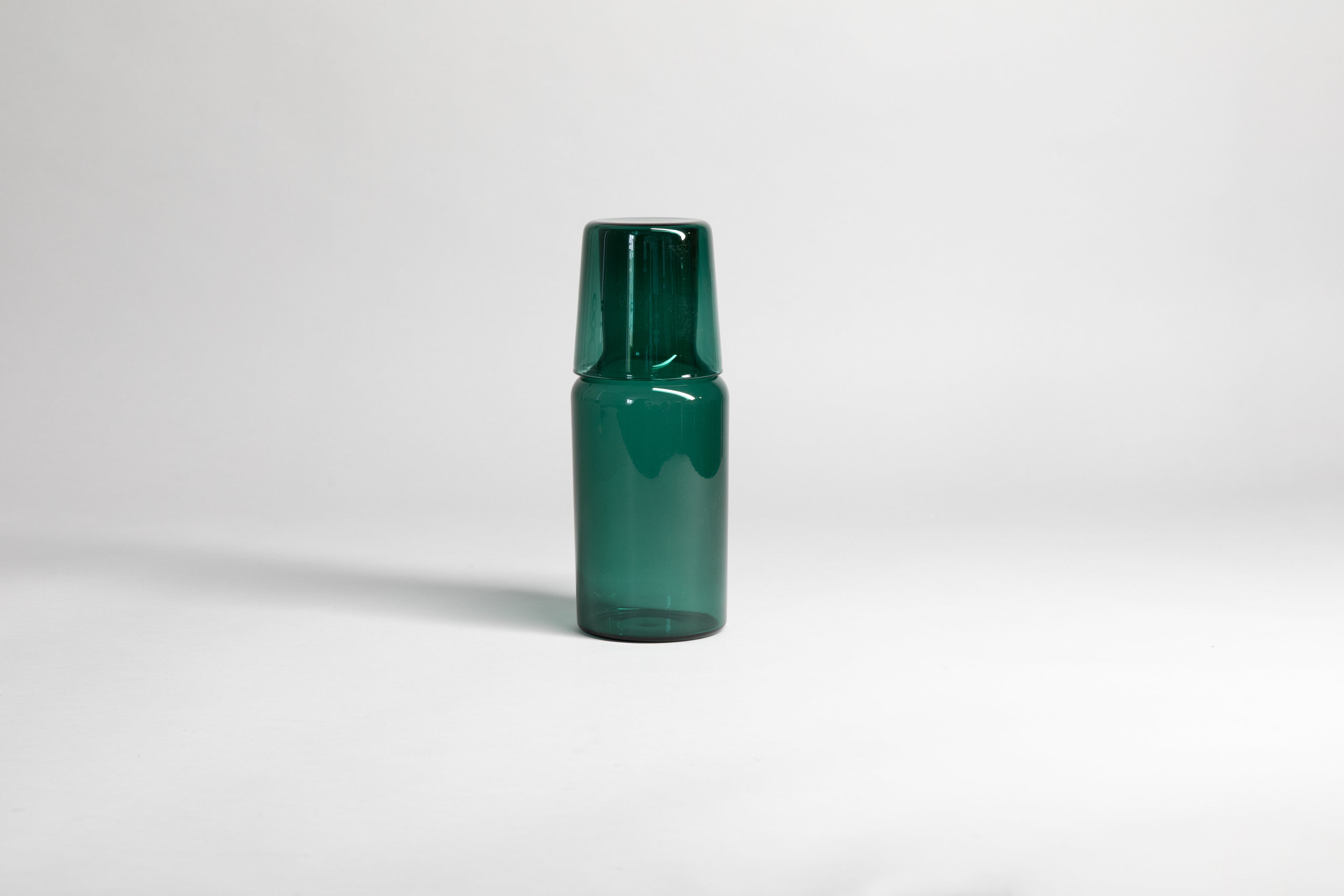 Transparent green carafe with matching glass cup flipped upside down on carafe top of carafe. Set on a light gray background